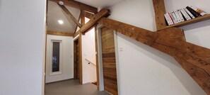 A hallway with exposed wooden beams, a white door, and a bookshelf with books. - 20% off on the first Sunday of All Saints' Day. Large 130-square-meter duplex • 6 bedrooms with made-up beds. Patio & Parking Lot (La Bresse)
