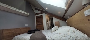 A bedroom with a sloped ceiling, wooden headboard, and a skylight. - 20% off on the first Sunday of All Saints' Day. Large 130-square-meter duplex • 6 bedrooms with made-up beds. Patio & Parking Lot (La Bresse)