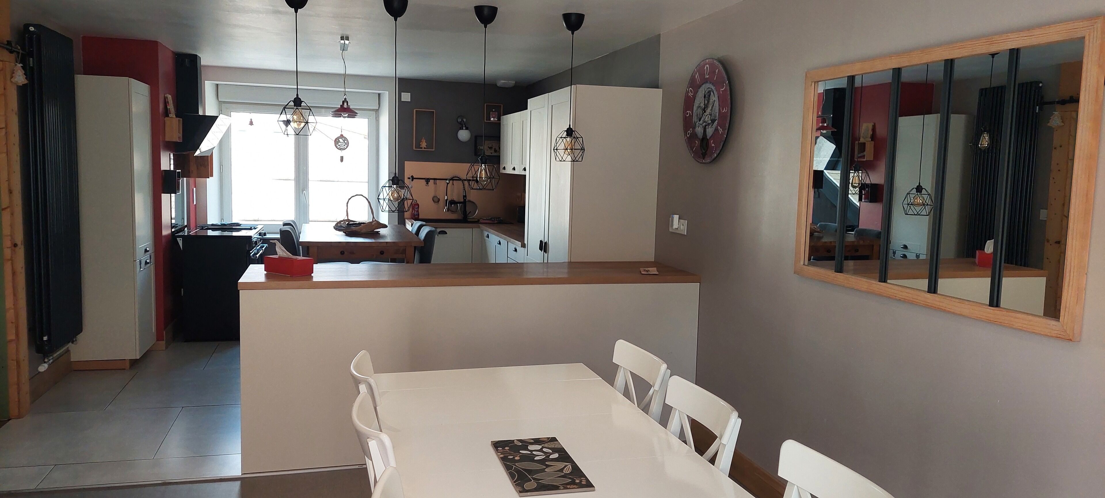 Cozinha moderna com armários brancos, bancada de madeira e luminárias pendentes. Há uma área de jantar com mesa e cadeiras brancas.