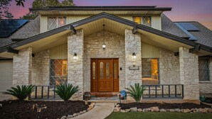 A two-story house with a stone facade, a wooden front door, and a covered porch. - Resort Oasis w/ Pool | Hot Tub | Mini Golf & Games (San Antonio)