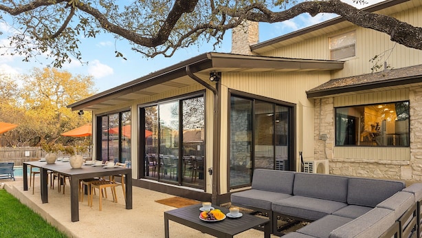 An outdoor patio with a dining table, a sofa, and a pool in the background. - Resort Oasis w/ Pool | Hot Tub | Mini Golf & Games (San Antonio)