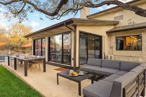 An outdoor patio with a dining table, a sofa, and a pool in the background. - Resort Oasis w/ Pool | Hot Tub | Mini Golf & Games (San Antonio)