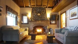 A cozy living room with two sofas, a fireplace, and a stone accent wall. - Secluded Forest Cabin in Rhododendron near Mt Hood Village in Oregon (Rhododendron)