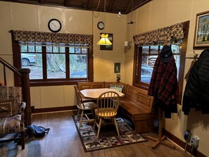 A dining area with a wooden table and chairs, a bench, a clock, and a window with a view of the outdoors. - Secluded Forest Cabin in Rhododendron near Mt Hood Village in Oregon (Rhododendron)