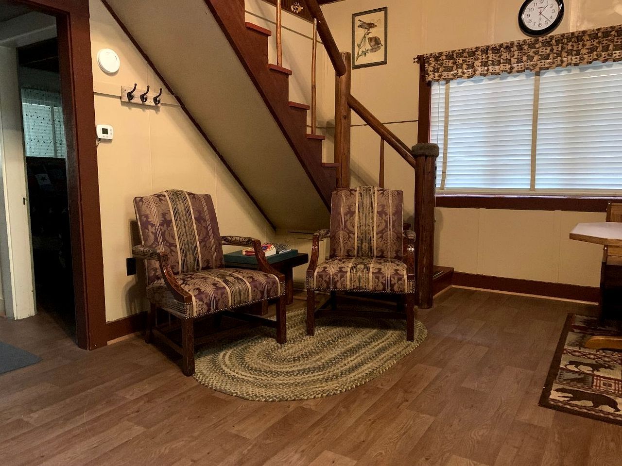A room with a wooden staircase, two patterned chairs, a small table, and a clock on the wall.