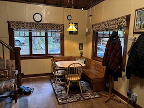 A dining area with a wooden table and chairs, a bench, a clock, and a window with a view of the outdoors. - Secluded Forest Cabin in Rhododendron near Mt Hood Village in Oregon (Rhododendron)