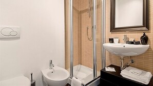 Une salle de bain avec une douche à parois de verre, un lavabo blanc, un miroir et un plan de toilette noir.
