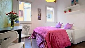 Une chambre à coucher avec un lit, une chaise, une table avec un vase et une fenêtre.
