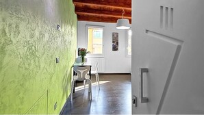 Un couloir avec un mur vert, un plafond en bois, une porte blanche et une fenêtre donnant sur l’extérieur.