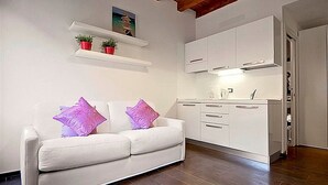 Un canapé blanc avec des coussins violets, une cuisine avec des meubles blancs et un plafond en bois.