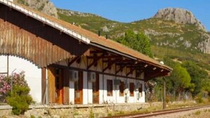 A traditional wooden building with a sloped roof, likely a train station, surrounded by a mountainous landscape.