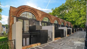Une rangée d’immeubles en briques, dotés de fenêtres en arc de cercle et bordée d’un chemin pavé de pierres.