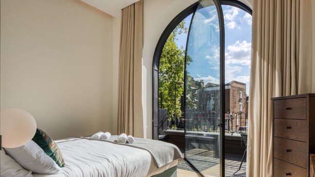 Une chambre avec une grande fenêtre, un lit, une commode et une vue sur l’extérieur.