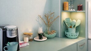 Una cocina con cafetera, frascos, un bol con ramas y una cesta con utensilios.