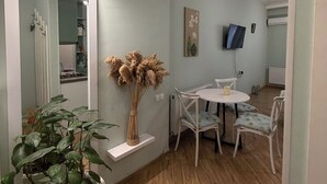 Una sala moderna con comedor, una planta grande en maceta y un televisor de pantalla plana montado en la pared.