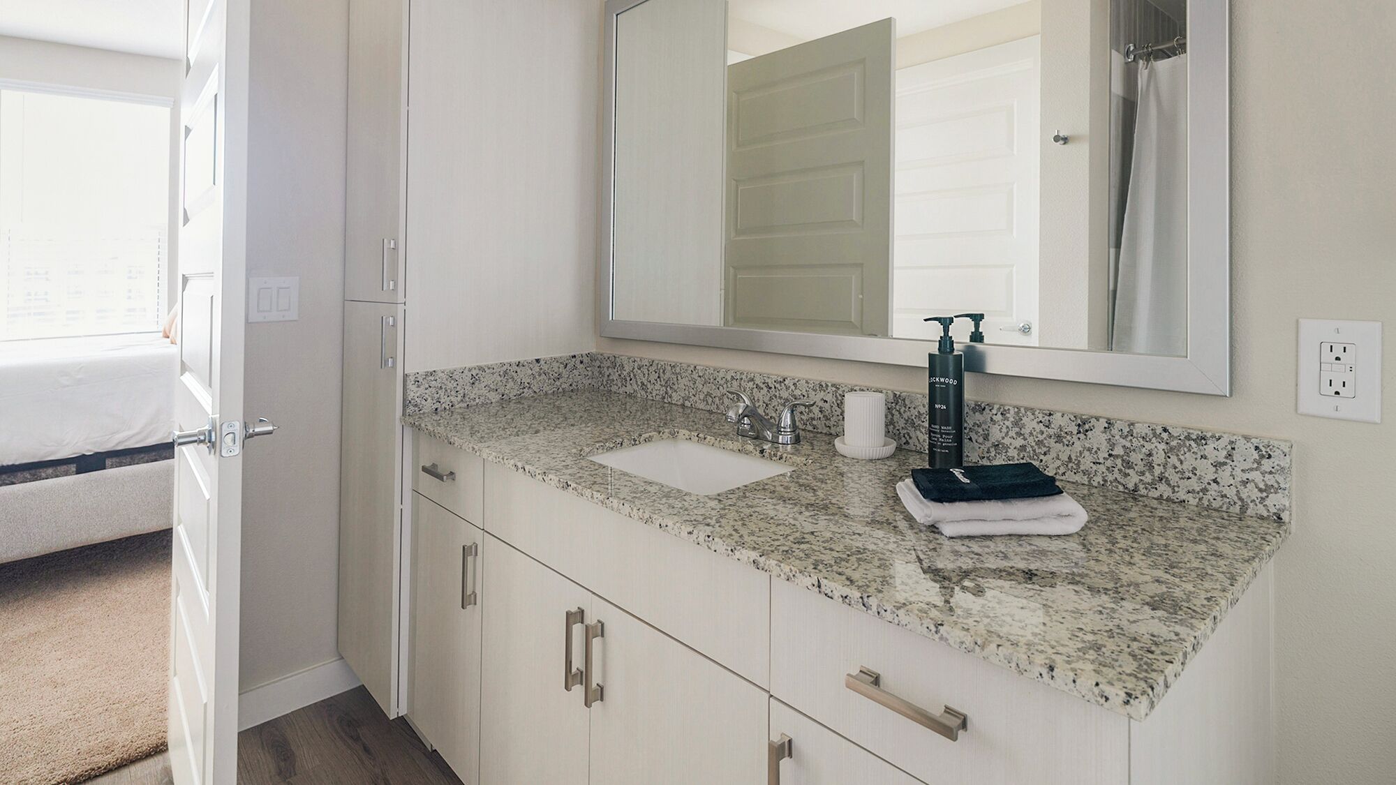 A modern bathroom with a granite countertop, two sinks, a large mirror, and a towel rack.