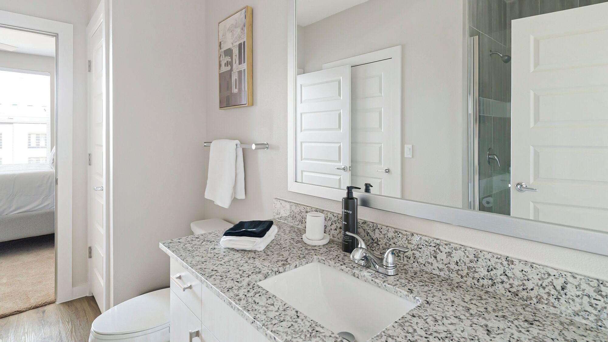 Un baño moderno con encimera de granito, un lavabo blanco, un espejo y una zona de ducha.