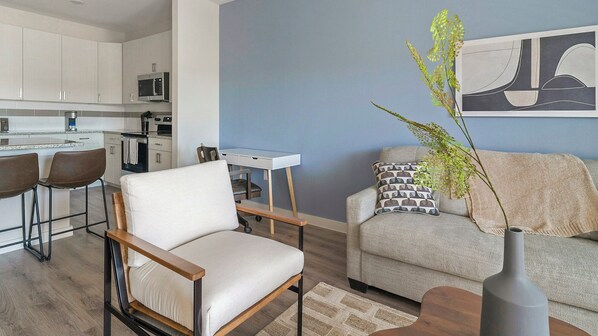 Una sala de estar moderna con un sofá blanco, una silla de madera, una mesa de comedor y una cocina con armarios blancos y un microondas.