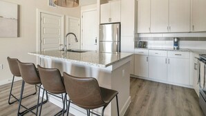 Una cocina moderna con una isla central, taburetes de bar, electrodomésticos de acero inoxidable y armarios blancos.