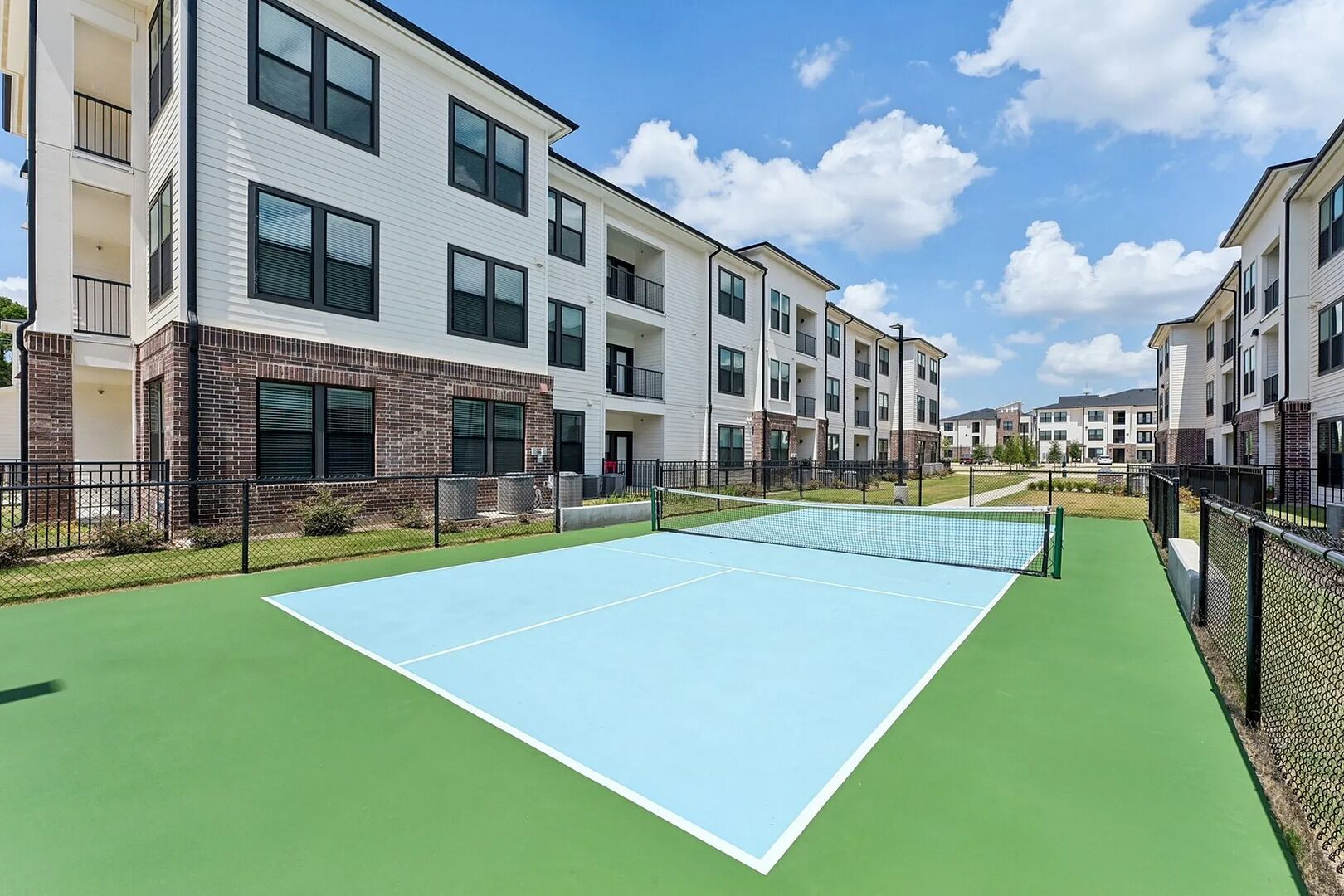 Una cancha de tenis rodeada de edificios residenciales con balcones.