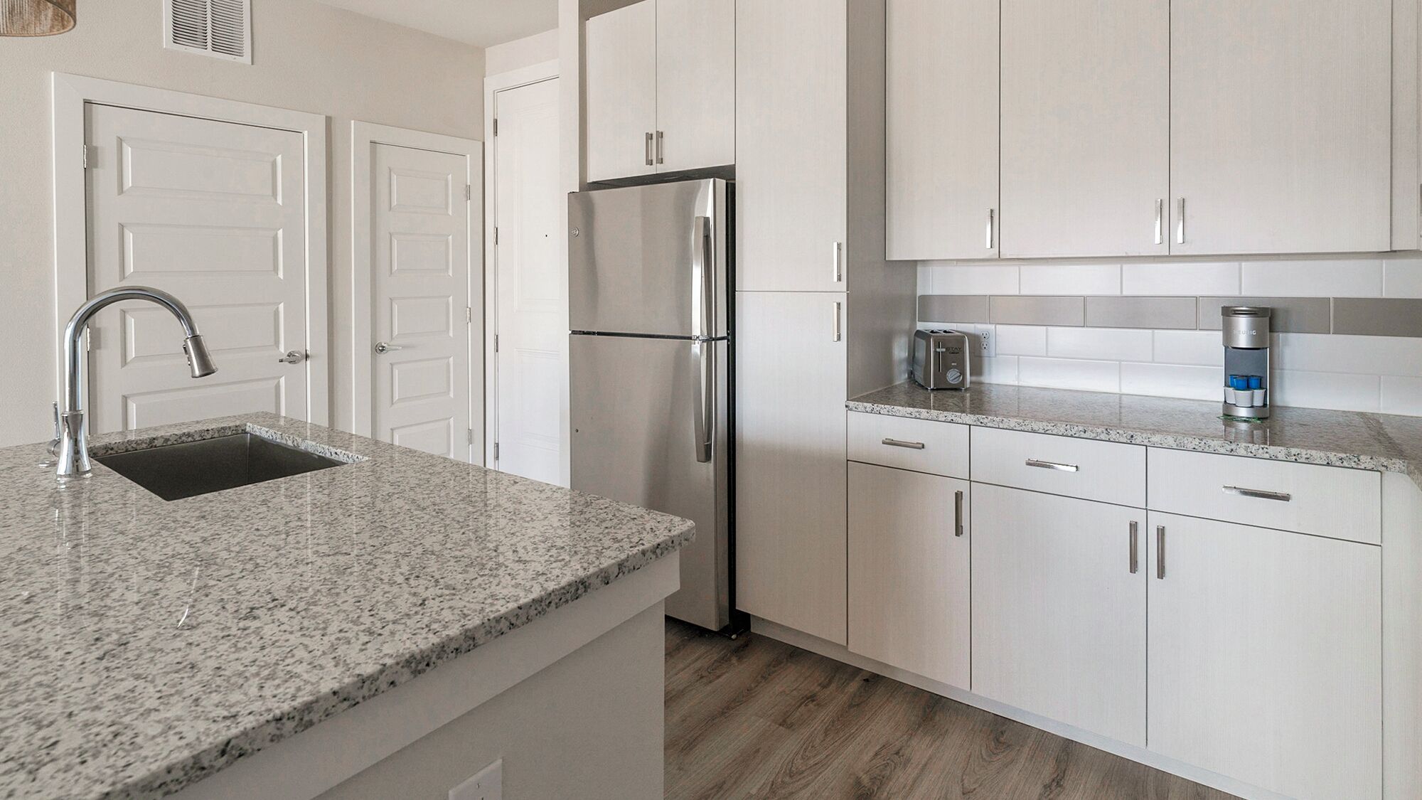 A modern kitchen with granite countertops, stainless steel appliances, and white cabinetry.