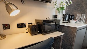 A kitchen with a microwave, toaster, and coffee maker on the counter. There is a vase with flowers on the wall and a chair in the foreground. - Howth Harbour Cosy Retreat (Howth)