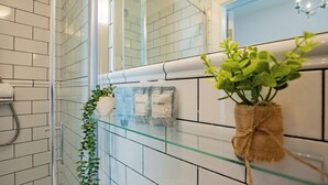 A bathroom with white tiled walls, a glass shower enclosure, and a small potted plant on a glass shelf. - Howth Harbour Cosy Retreat (Howth)