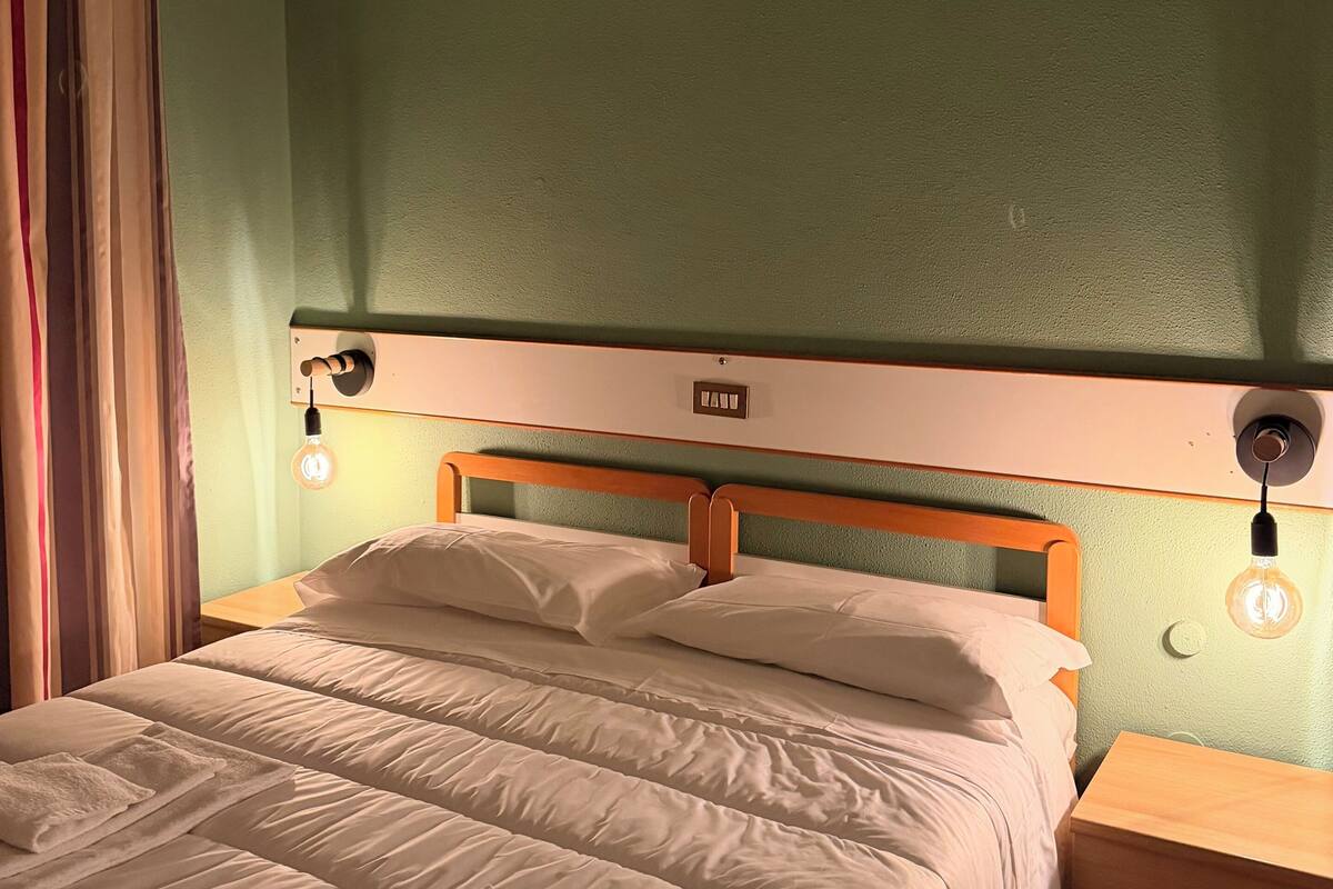 A neatly made bed with white linens, a wooden headboard, and two bedside lamps.
