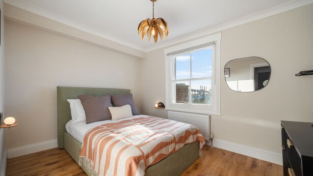 Ein Schlafzimmer mit Bett, Fenster, Spiegel und Kommode.