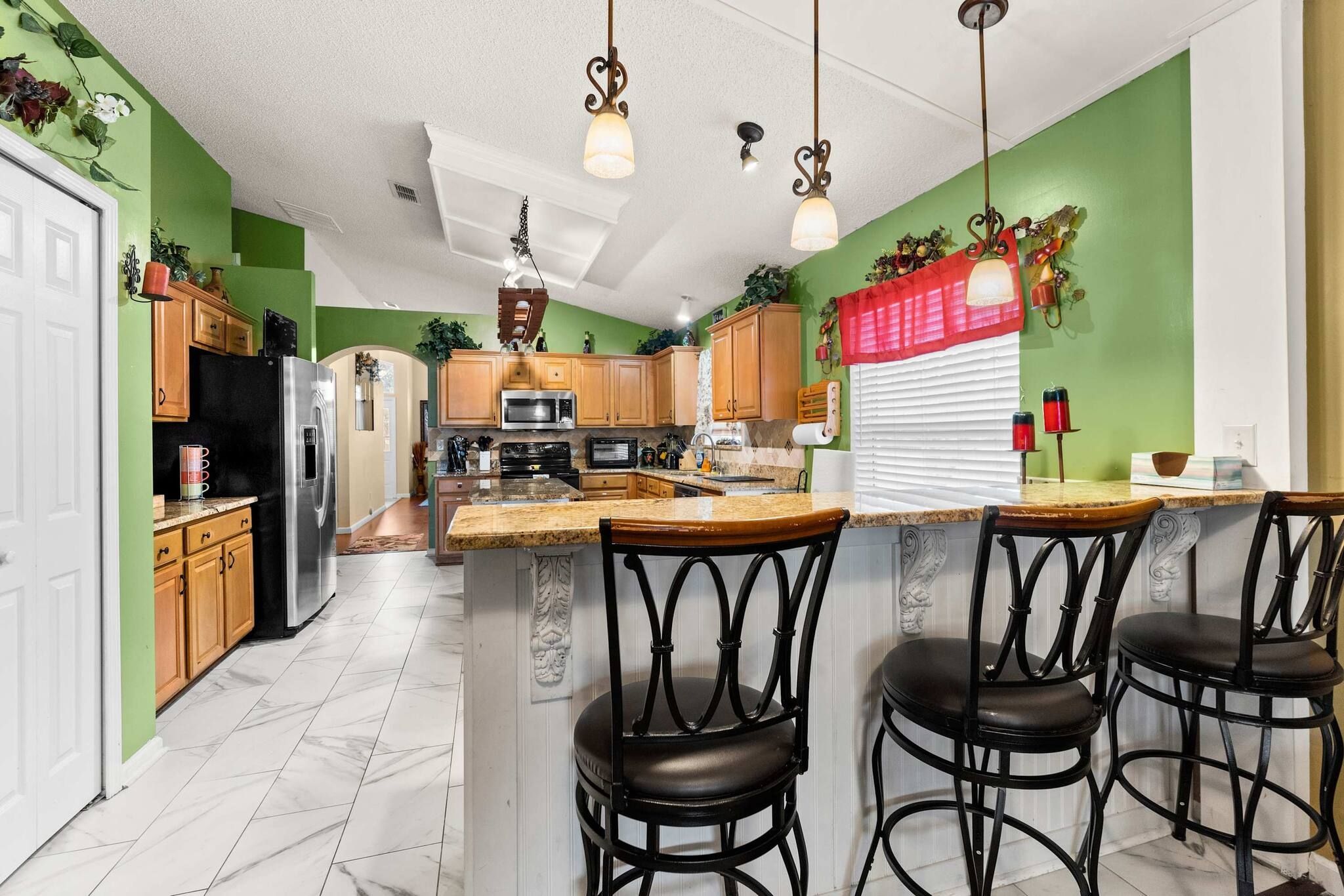 Una cocina con una isla central, taburetes de bar y un refrigerador.