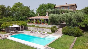 Ein Pool mit Liegestühlen, eine kleine überdachte Sitzgelegenheit und ein Steinhaus mit Ziegeldach.