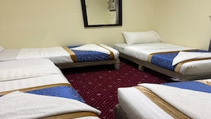 A hotel room with four beds arranged in a square layout, a red patterned carpet, and a wall-mounted mirror. - Al-Orabi Hotel (Makkah)