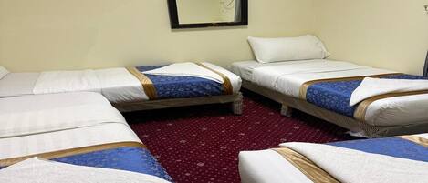A hotel room with four beds arranged in a square layout, a red patterned carpet, and a wall-mounted mirror.