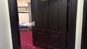 A room with a bed, a small table, and a door with a sign above it. - Al-Orabi Hotel (Makkah)
