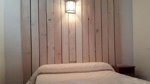 Un dormitorio con pared de listones de madera, una cama con ropa de cama blanca y una mesita de noche con lámpara.