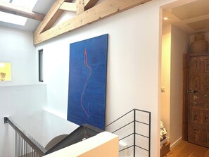 A modern interior with a wooden ceiling, a blue abstract painting, a staircase, and a traditional wooden door. - Village house in the heart of Puyricard with swimming pool (Aix-en-Provence)