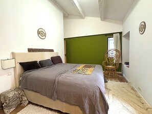 Un dormitorio con cama, una silla y un panel divisor verde.