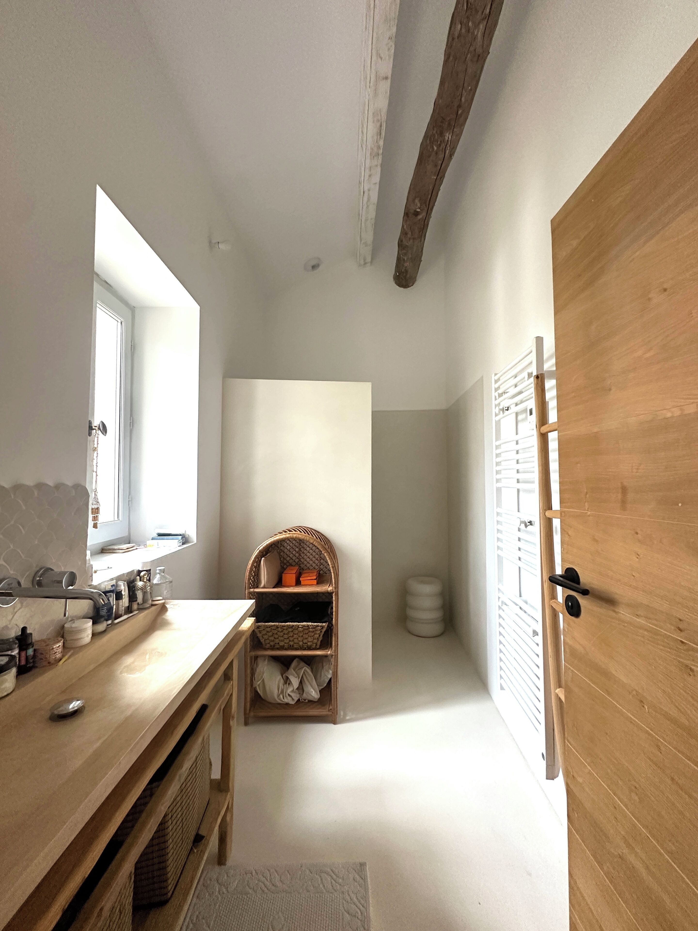 Un baño estrecho con tocador de madera, repisa de mimbre y puerta de madera.