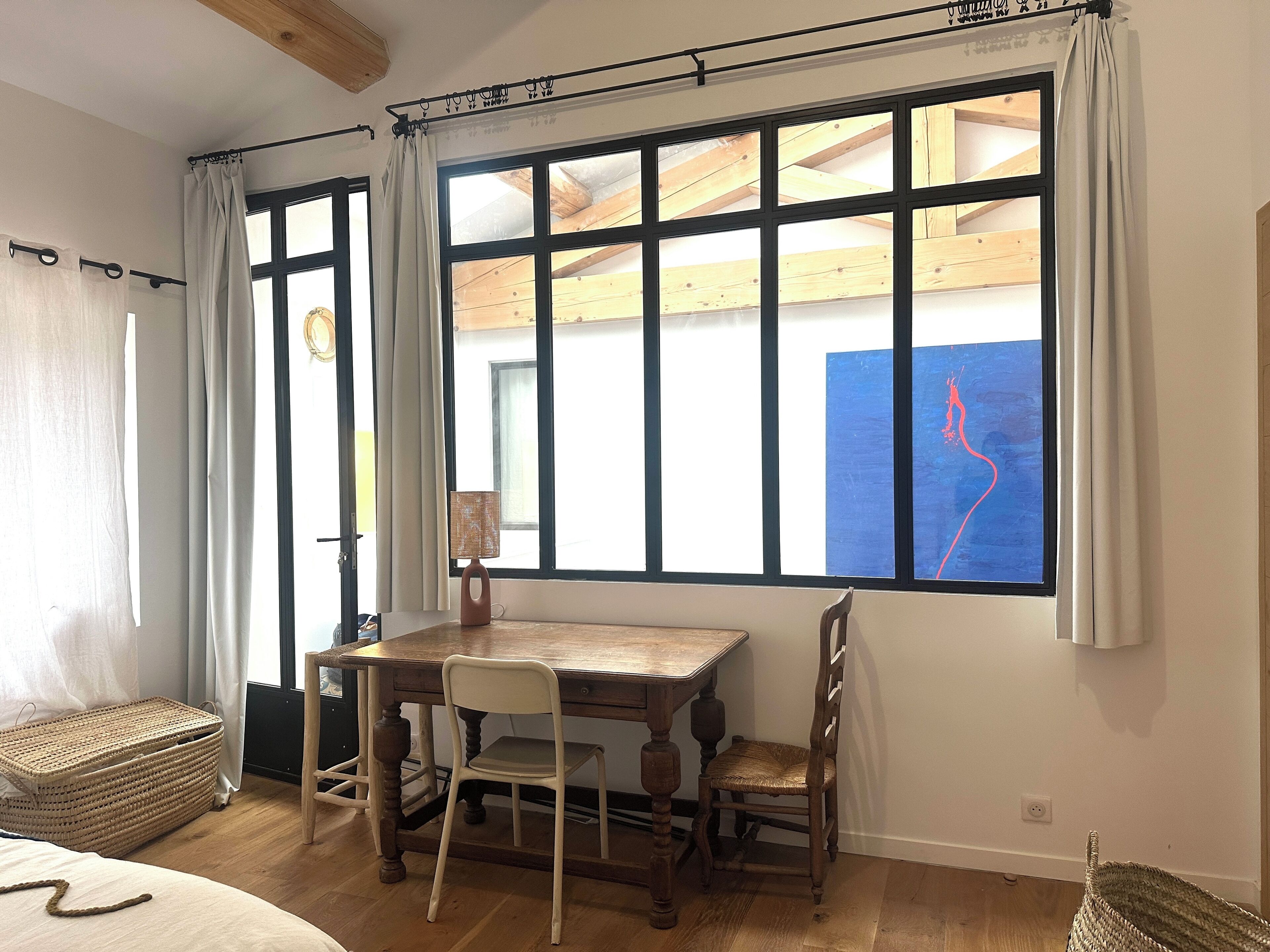 Un comedor con una mesa y sillas de madera, una cesta de mimbre y una ventana con cortinas.