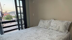 Ein Schlafzimmer mit einem Bett, einem Fenster mit Blick auf die Straße und einer Klimaanlage an der Wand.