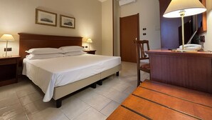 A hotel room with a bed, two bedside tables with lamps, a wooden desk with a lamp, and a chair. - Naples Park Hotel (Marigliano)