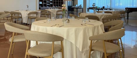 A dining area with round tables, chairs, and a piano.