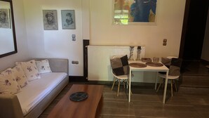 Un salon comprenant un canapé, une table basse et un coin repas avec des chaises et une table. Des œuvres d’art encadrées ornent le mur.
