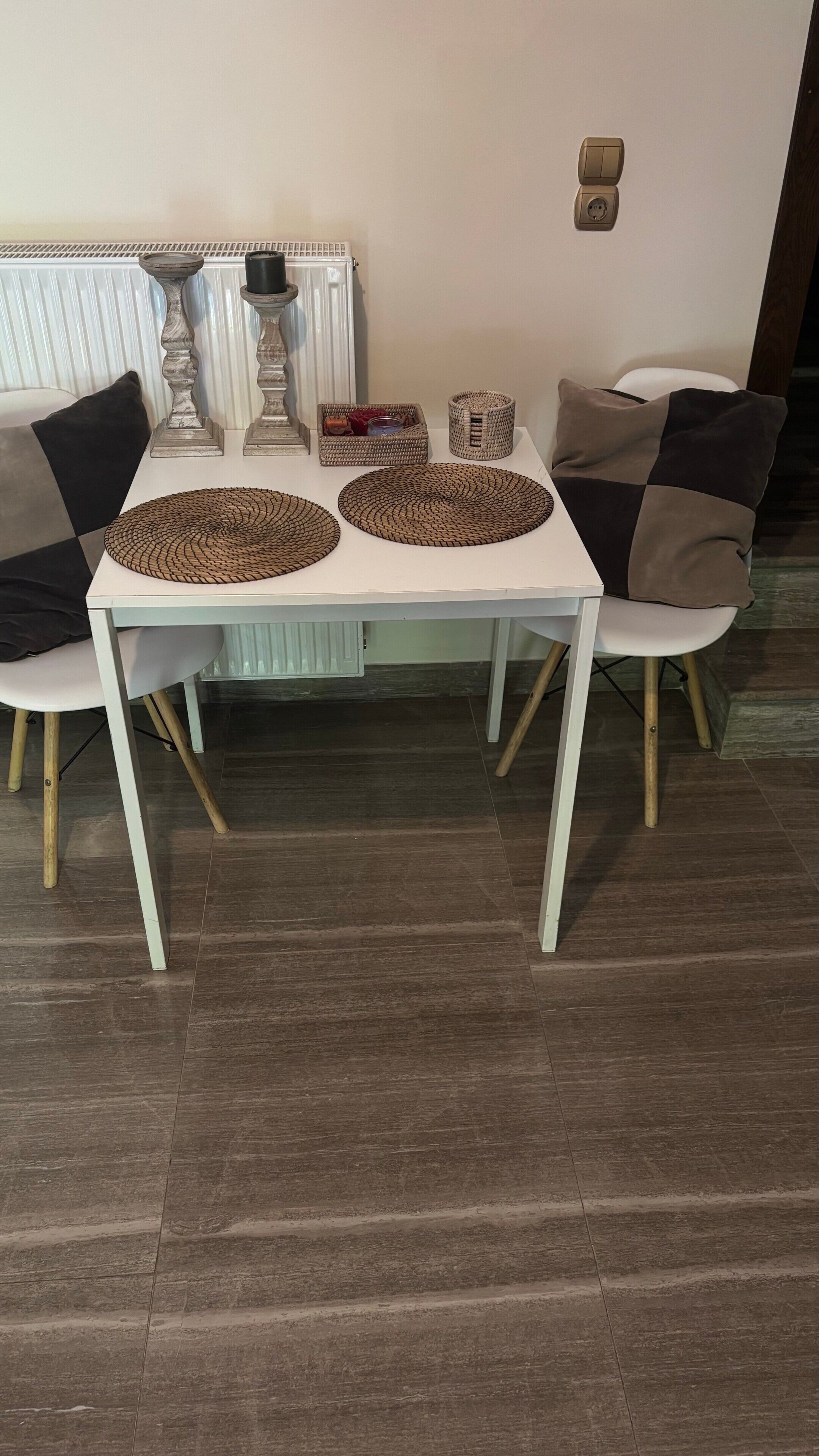 Une table à manger avec des sets de table en osier, deux chaises, un radiateur et une prise électrique murale.