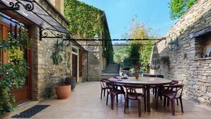 Un bâtiment en pierre doté d’un patio comprenant une table ronde et des chaises.