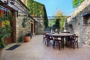 A stone building with a patio area featuring a round table and chairs. - Maison des papillons Daglan – Spacious Family Home with Pool in Village Center (Daglan)