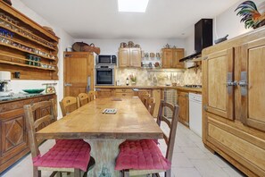 A kitchen with wooden cabinets, a dining table, chairs, a microwave, an oven, and a dishwasher. - Maison des papillons Daglan – Spacious Family Home with Pool in Village Center (Daglan)