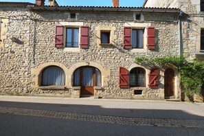A stone building with arched windows and red shutters, featuring a cobblestone street in front. - Maison des papillons Daglan – Spacious Family Home with Pool in Village Center (Daglan)