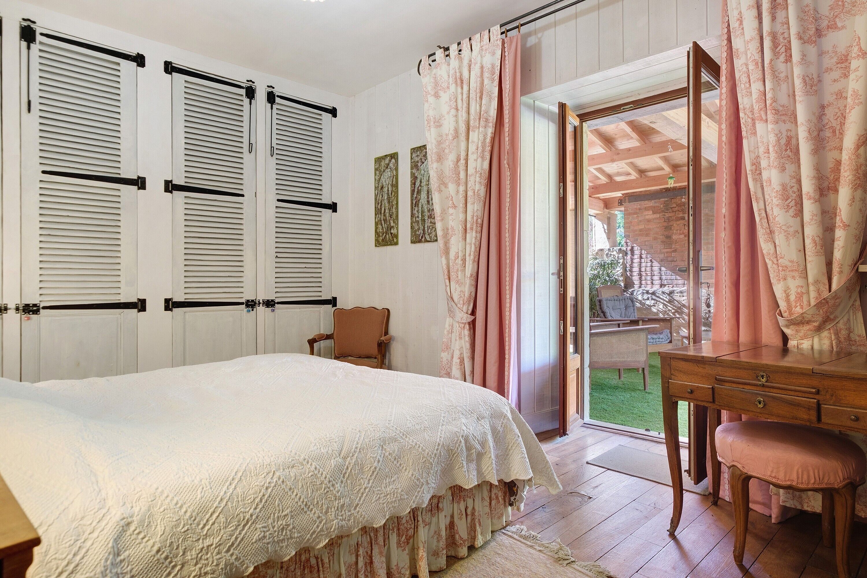 A bedroom with a bed, a wooden desk, a chair, and a sliding glass door leading to a balcony.