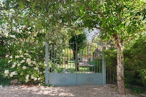 A gated garden area with a gravel path, surrounded by lush greenery and white flowering plants. - Maison des papillons Daglan – Spacious Family Home with Pool in Village Center (Daglan)